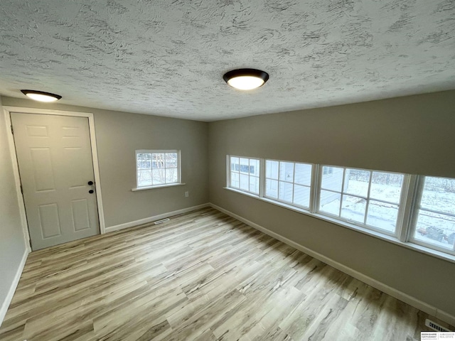 spare room with light wood-type flooring, baseboards, and a textured ceiling