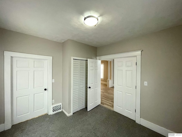 unfurnished bedroom featuring baseboards, dark colored carpet, and a closet