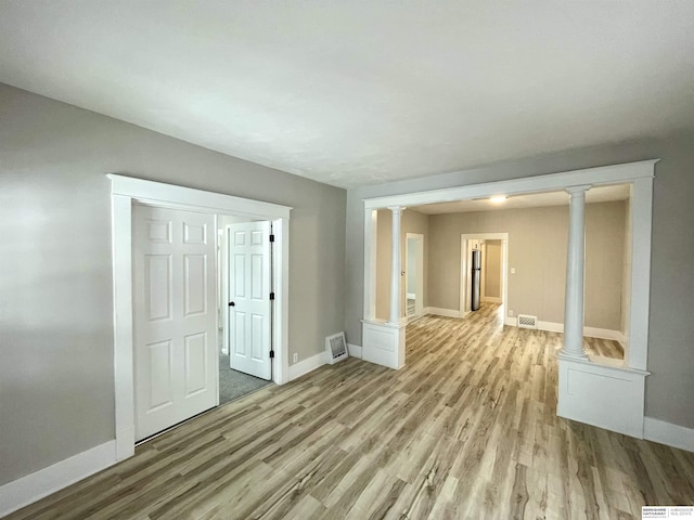 unfurnished room featuring decorative columns, baseboards, and light wood-type flooring