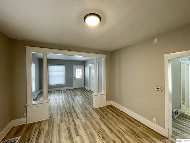 empty room with visible vents, light wood-style flooring, baseboards, and decorative columns