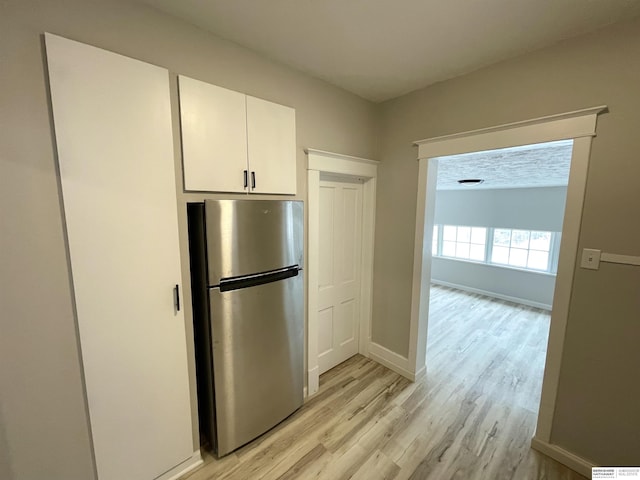 kitchen with white cabinetry, light wood-style floors, baseboards, and freestanding refrigerator