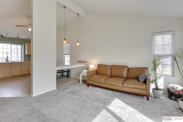 living area featuring a ceiling fan, track lighting, baseboards, light colored carpet, and vaulted ceiling with beams