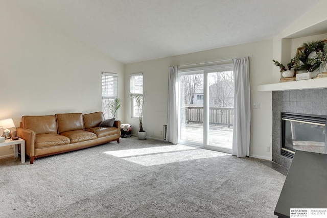 living area with a wealth of natural light, a tile fireplace, lofted ceiling, and carpet floors