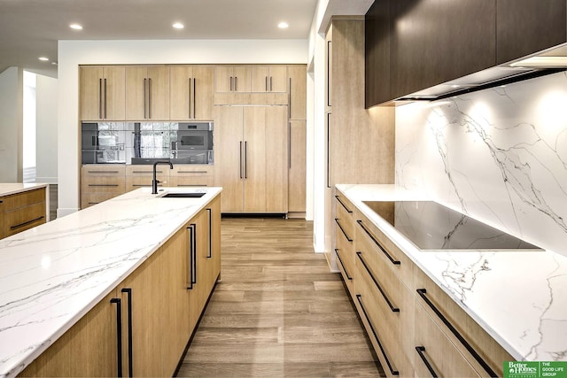 kitchen featuring tasteful backsplash, light stone countertops, paneled built in fridge, black electric cooktop, and a sink