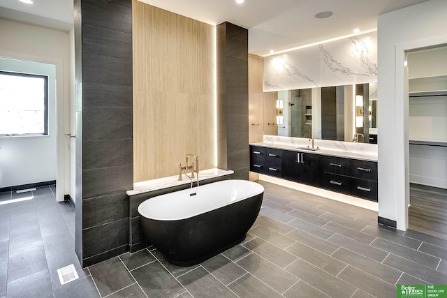 full bathroom with a soaking tub, tile walls, and vanity