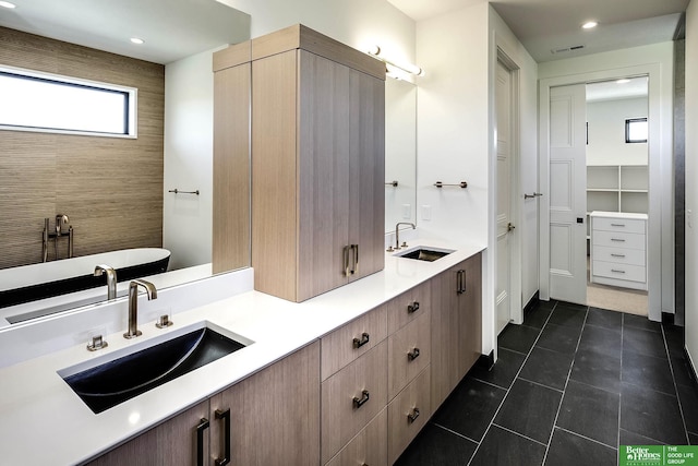 bathroom with tile patterned flooring, a soaking tub, double vanity, and a sink