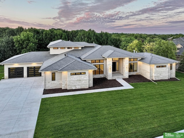 view of front of property featuring stucco siding, driveway, a yard, stone siding, and an attached garage