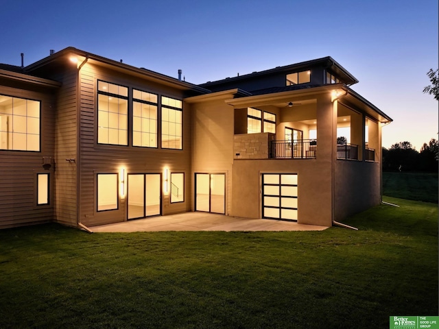 back of house at dusk with a yard, a balcony, and a patio area