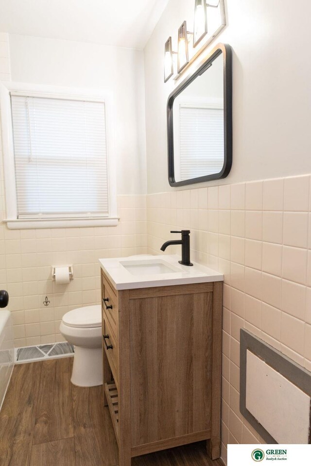 bathroom featuring visible vents, toilet, wood finished floors, tile walls, and vanity