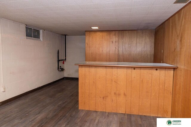 bar with concrete block wall, a bar, wood walls, and dark wood-style flooring