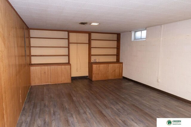 basement with concrete block wall, dark wood-style floors, and visible vents