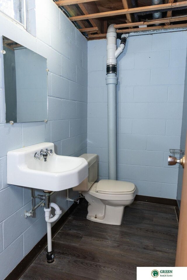 half bath with a sink, toilet, wood finished floors, and concrete block wall