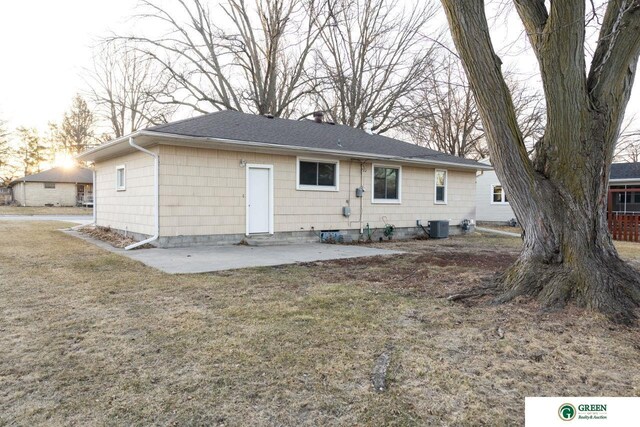 back of house featuring central air condition unit, a patio, a yard, a shingled roof, and a chimney