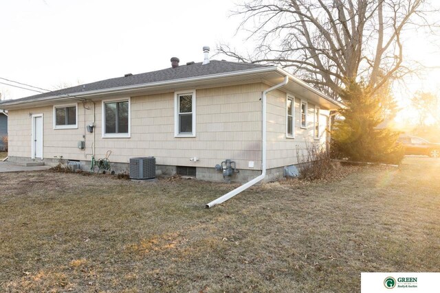 back of house with a yard, cooling unit, and a shingled roof