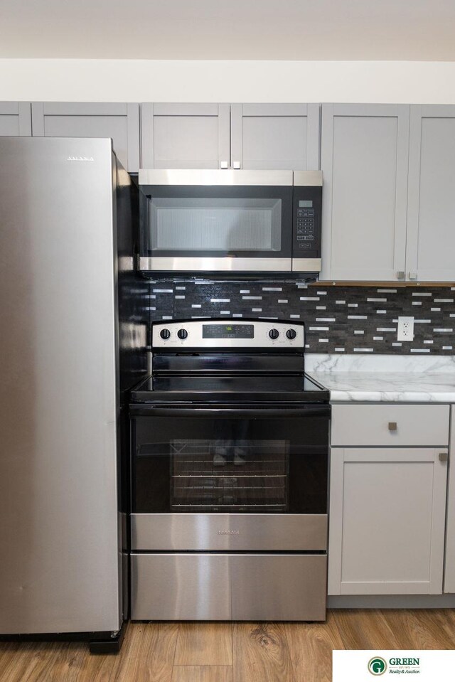 kitchen with tasteful backsplash, appliances with stainless steel finishes, light wood-type flooring, and light stone counters