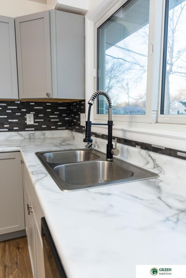 details featuring backsplash, light stone countertops, dishwashing machine, wood finished floors, and a sink