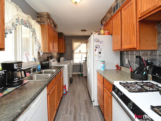 kitchen featuring a sink, backsplash, white appliances, separate washer and dryer, and brown cabinetry