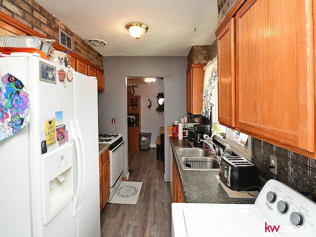 kitchen with a sink, white appliances, washer / dryer, and brown cabinetry