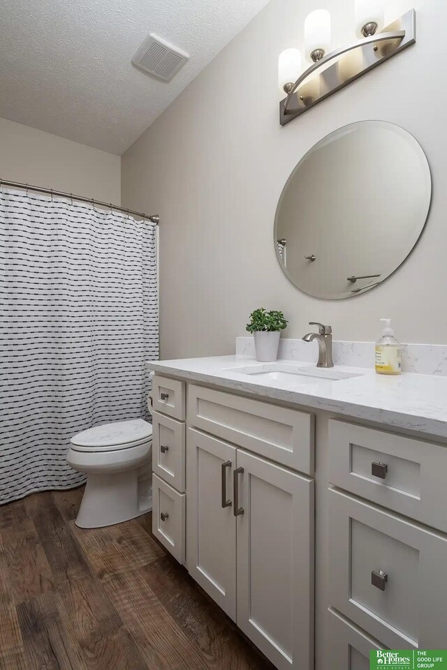 bathroom featuring visible vents, toilet, vanity, wood finished floors, and a textured ceiling