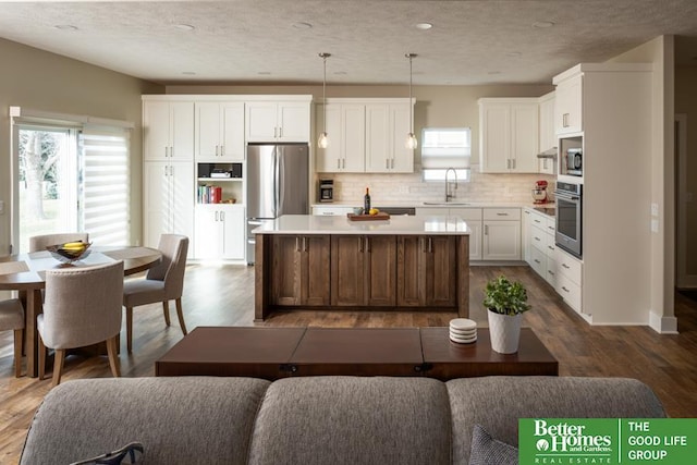 kitchen featuring dark wood finished floors, a sink, appliances with stainless steel finishes, white cabinetry, and a center island