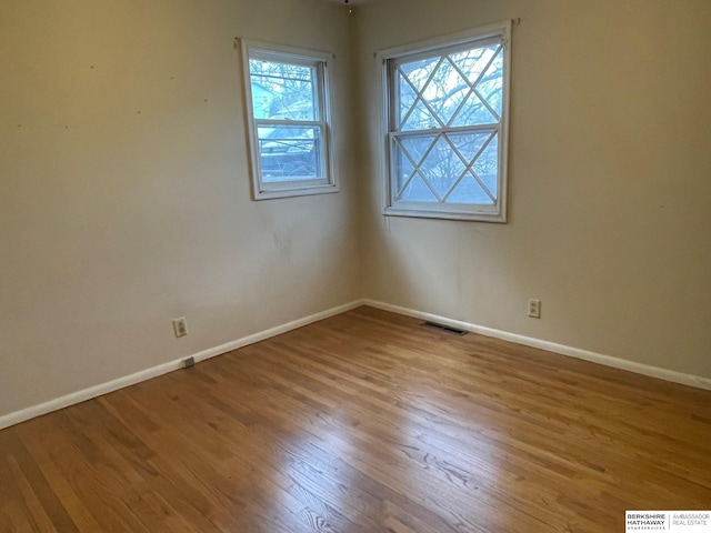 empty room featuring wood finished floors, visible vents, and baseboards