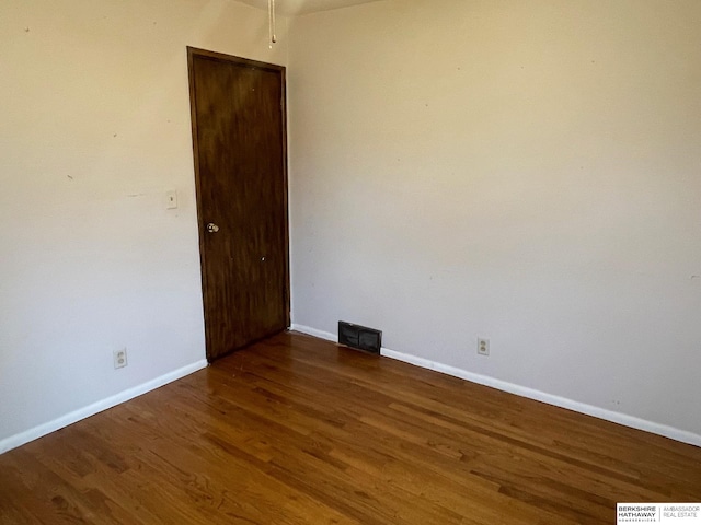 empty room with wood finished floors, visible vents, and baseboards