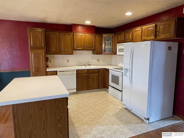 kitchen featuring white appliances, a sink, light countertops, glass insert cabinets, and brown cabinets