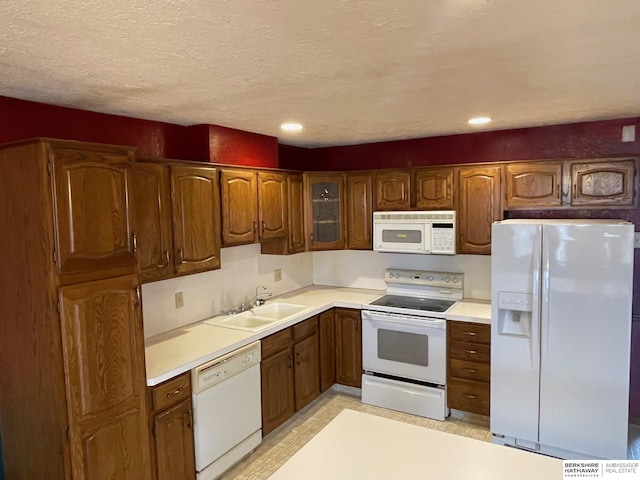 kitchen with light countertops, brown cabinetry, white appliances, a textured ceiling, and a sink