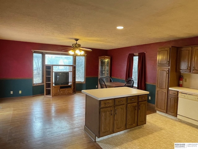 kitchen with a ceiling fan, a textured ceiling, a kitchen island, white dishwasher, and light countertops