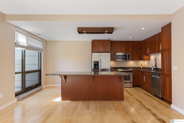 kitchen with light wood finished floors, a kitchen island, recessed lighting, stainless steel appliances, and a kitchen bar