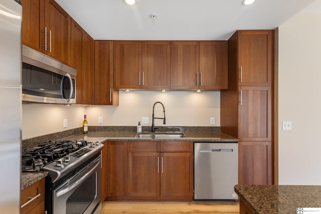 kitchen featuring dark stone countertops, brown cabinetry, recessed lighting, a sink, and stainless steel appliances