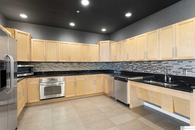 kitchen featuring light brown cabinets, a sink, decorative backsplash, stainless steel appliances, and dark countertops