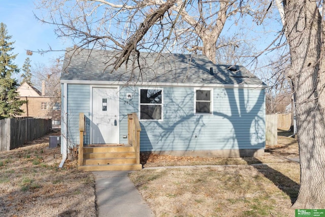 bungalow featuring cooling unit, fence, and roof with shingles