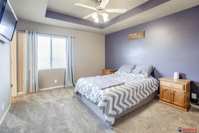 bedroom with light carpet, ceiling fan, baseboards, and a tray ceiling