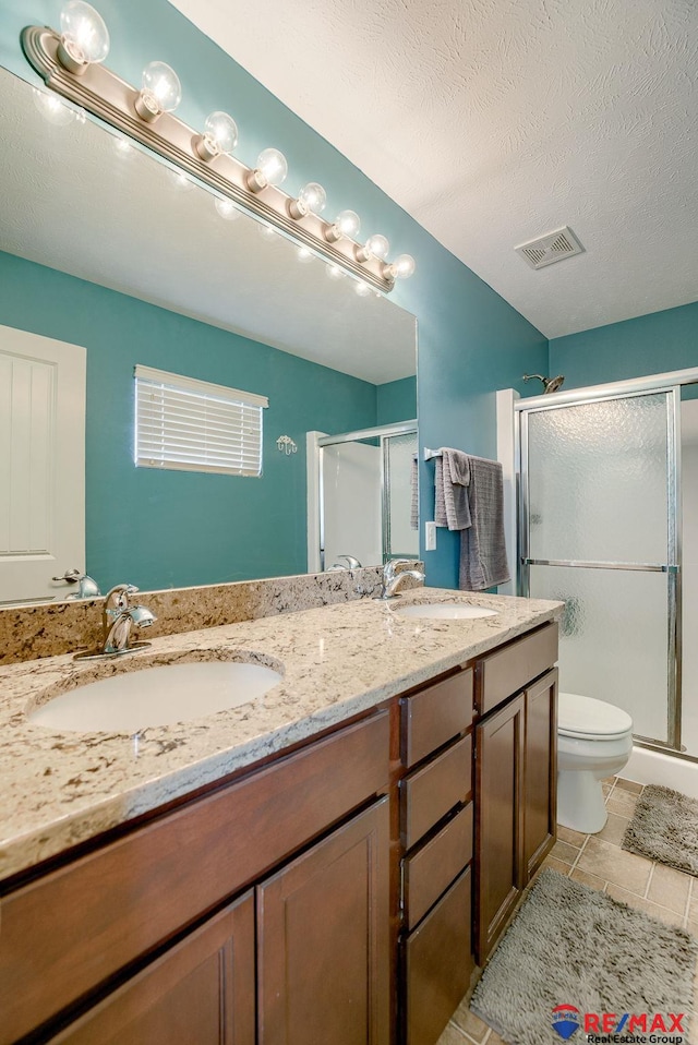 bathroom featuring a shower stall, toilet, double vanity, and a sink