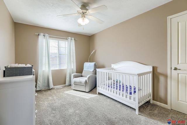 carpeted bedroom featuring baseboards, a nursery area, ceiling fan, and a textured ceiling