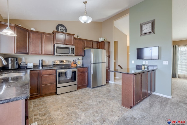 kitchen featuring dark stone counters, appliances with stainless steel finishes, a peninsula, hanging light fixtures, and a sink