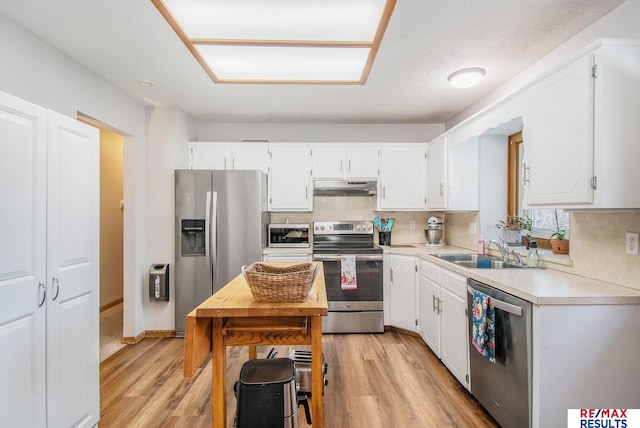 kitchen featuring under cabinet range hood, light wood-type flooring, light countertops, stainless steel appliances, and a sink