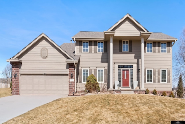 greek revival inspired property with brick siding, a front yard, an attached garage, and driveway