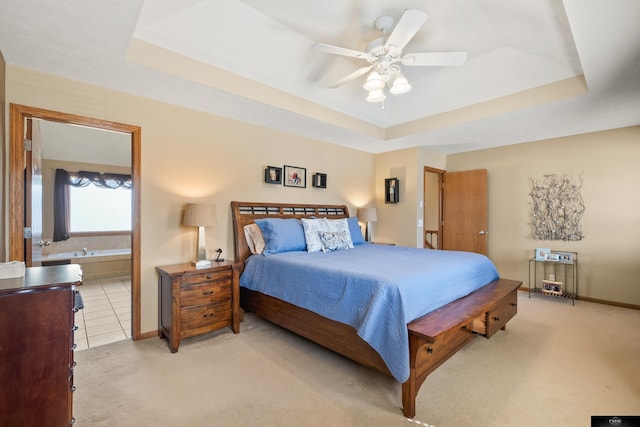 bedroom with baseboards, a raised ceiling, light carpet, and ensuite bath