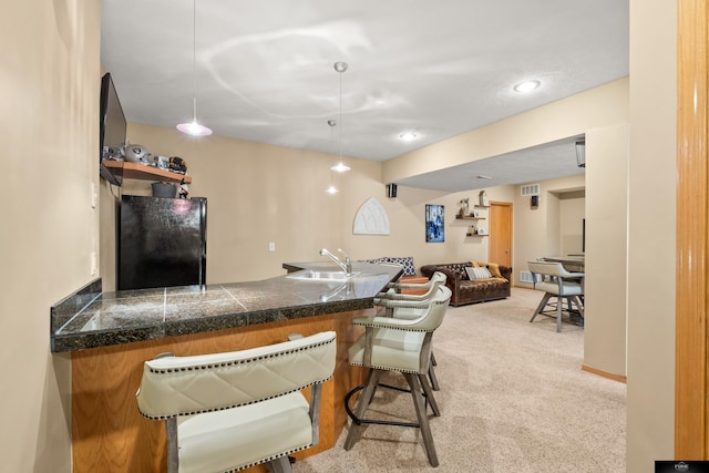 kitchen with freestanding refrigerator, a sink, tile counters, light carpet, and a kitchen bar