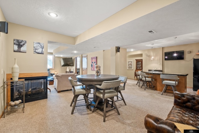 dining space with a multi sided fireplace, bar, a textured ceiling, and light colored carpet