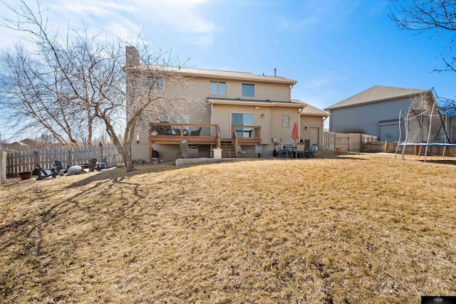 rear view of house featuring a deck, a trampoline, a fenced backyard, and a lawn