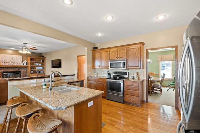 kitchen featuring tasteful backsplash, open floor plan, appliances with stainless steel finishes, brown cabinetry, and a sink