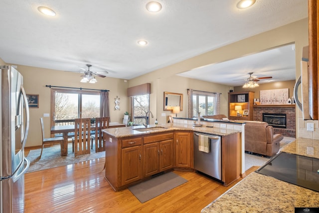 kitchen featuring light wood-type flooring, a fireplace, a sink, stainless steel appliances, and brown cabinets