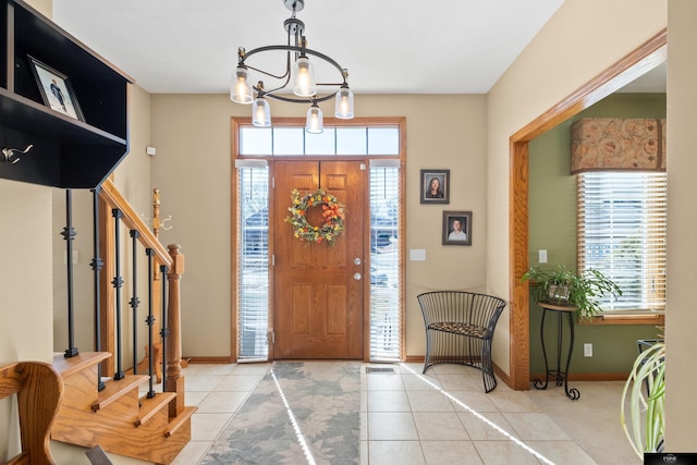 tiled foyer featuring a notable chandelier, stairs, and baseboards