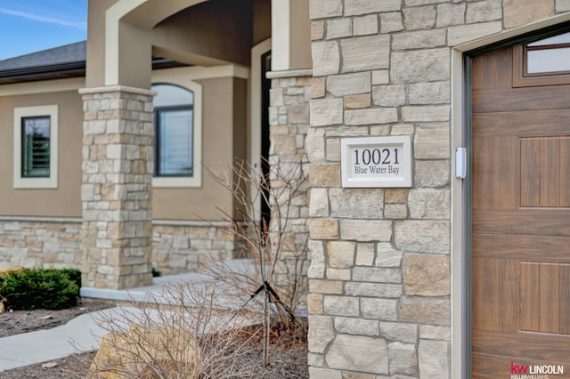 doorway to property featuring stone siding and a shingled roof