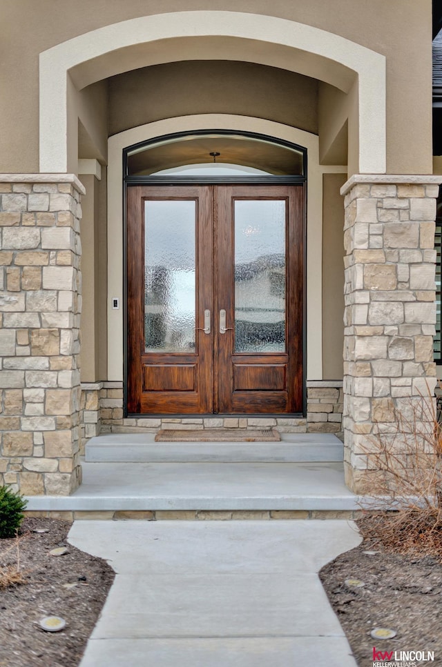 view of exterior entry with stucco siding, stone siding, and french doors