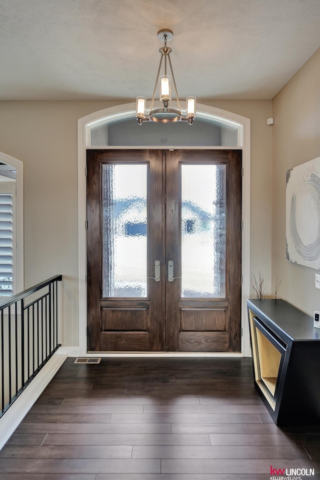 foyer with dark wood finished floors, an inviting chandelier, french doors, and visible vents