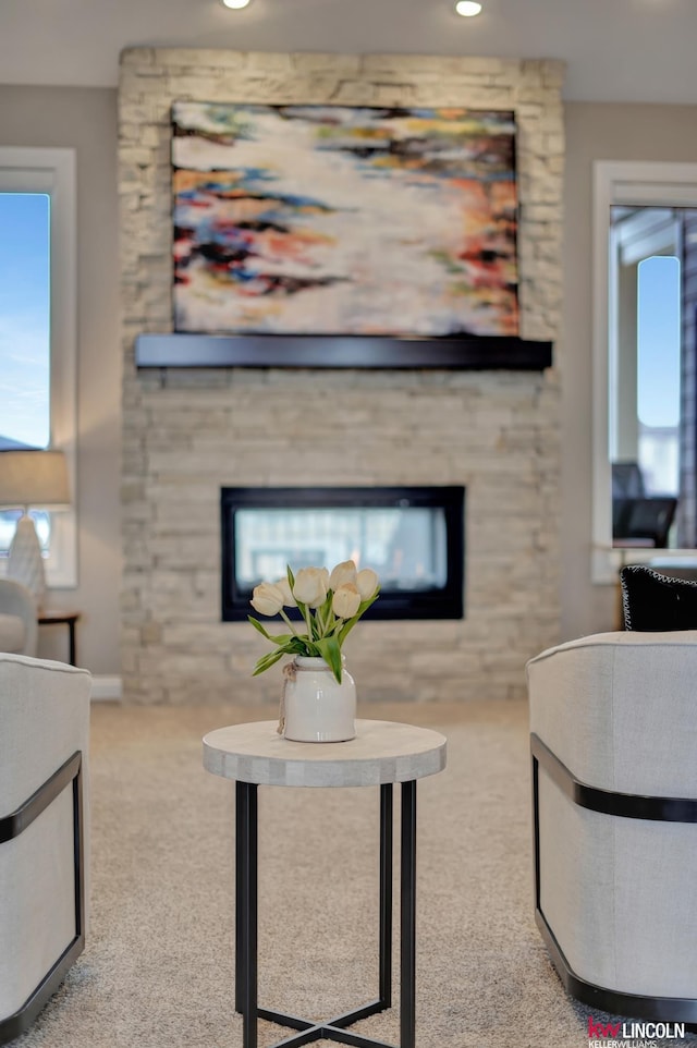 living area featuring a stone fireplace and carpet